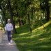 Elderly woman running along a riverside path in a green park, embracing fitness and nature.
